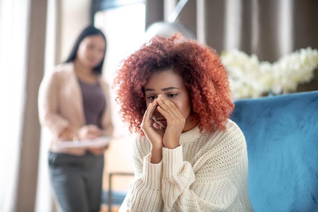 woman with hands over face, sitting on couch in front of other woman, wondering if she is feeling the symptoms of fentanyl overdose